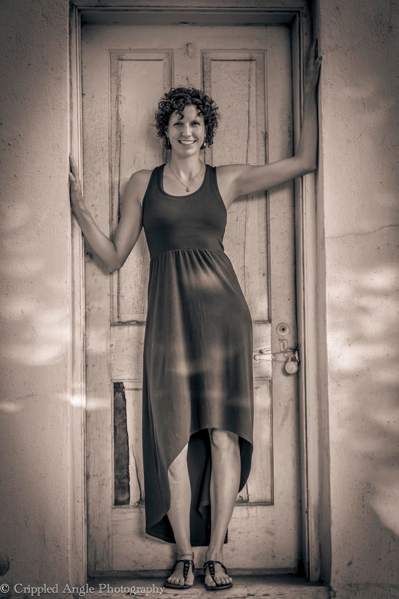 Black and white portrait showing a figure in a flowing dress standing in an old doorway.