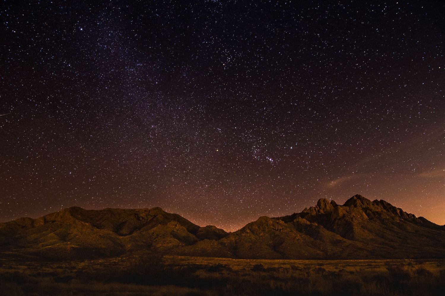 Desert mountain silhouettes under a starry night sky with dramatic rock formations.