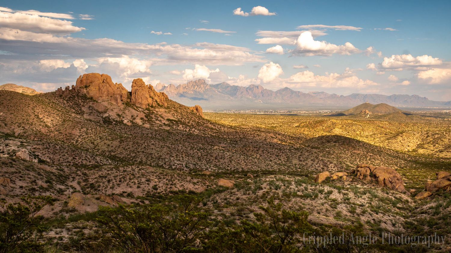 Desert landscape with dramatic rock formations and mountains under a blue sky with scattered clouds.