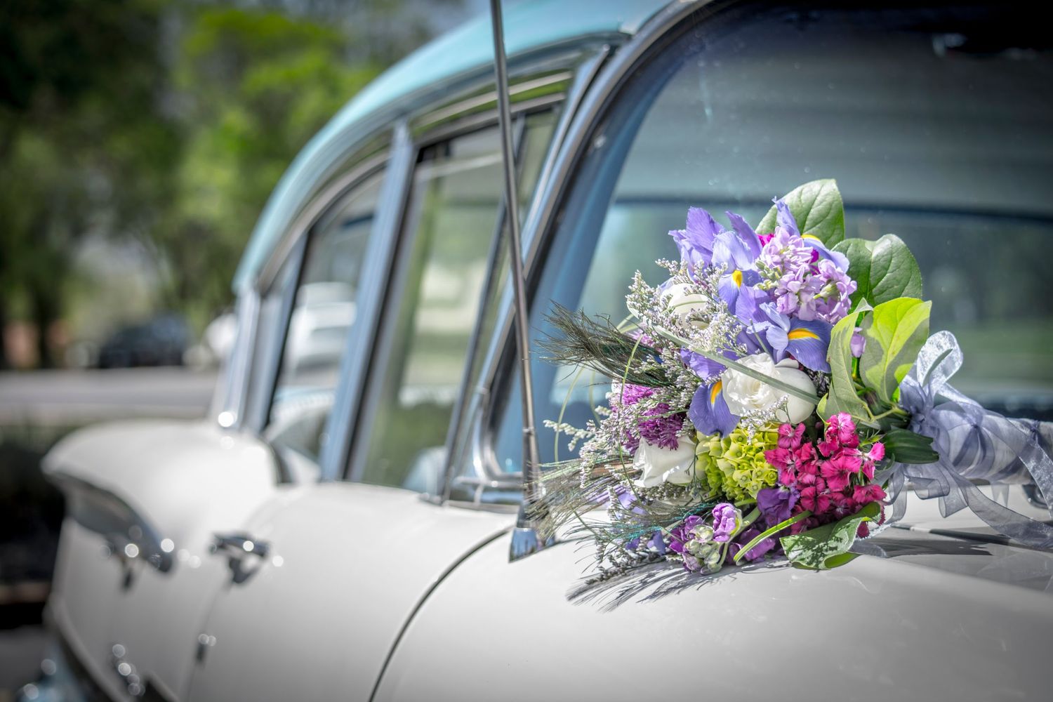 Purple and white wedding bouquet rests on vintage silver car during wedding celebration.