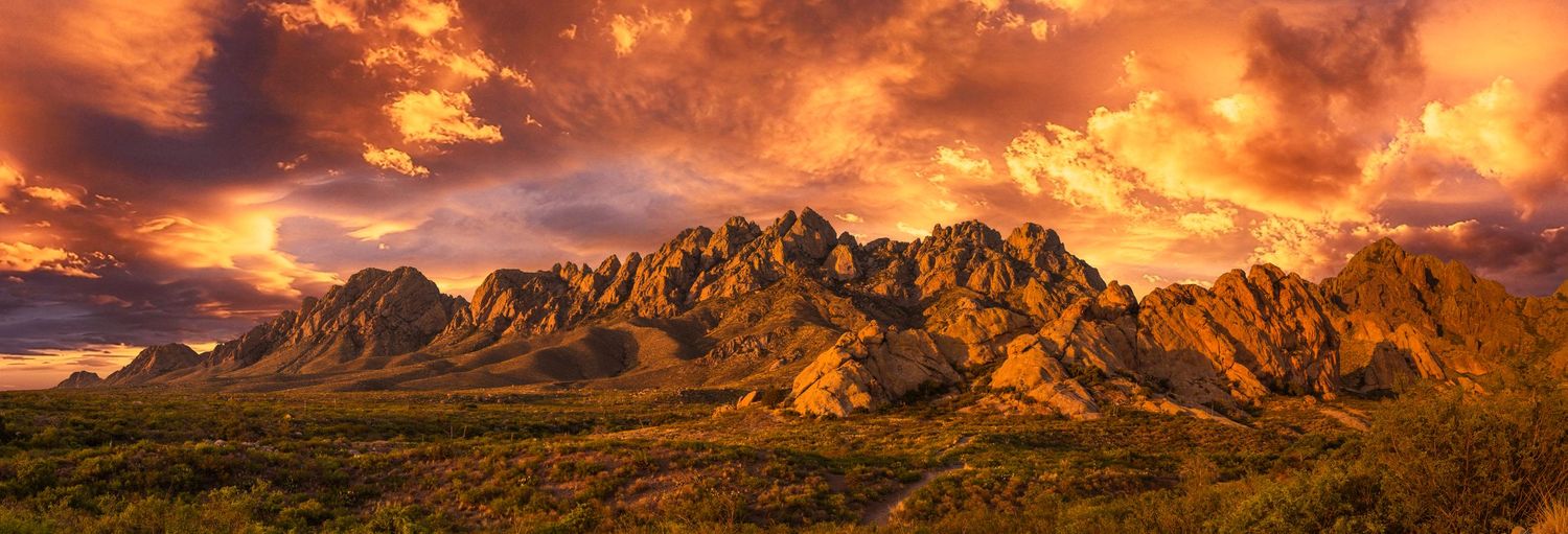Majestic mountain range glowing orange at sunset against a dramatic cloudy sky in the desert landscape.