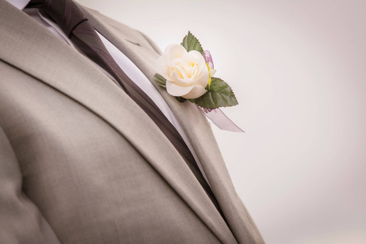 A cream rose boutonniere pinned to a light gray suit jacket.