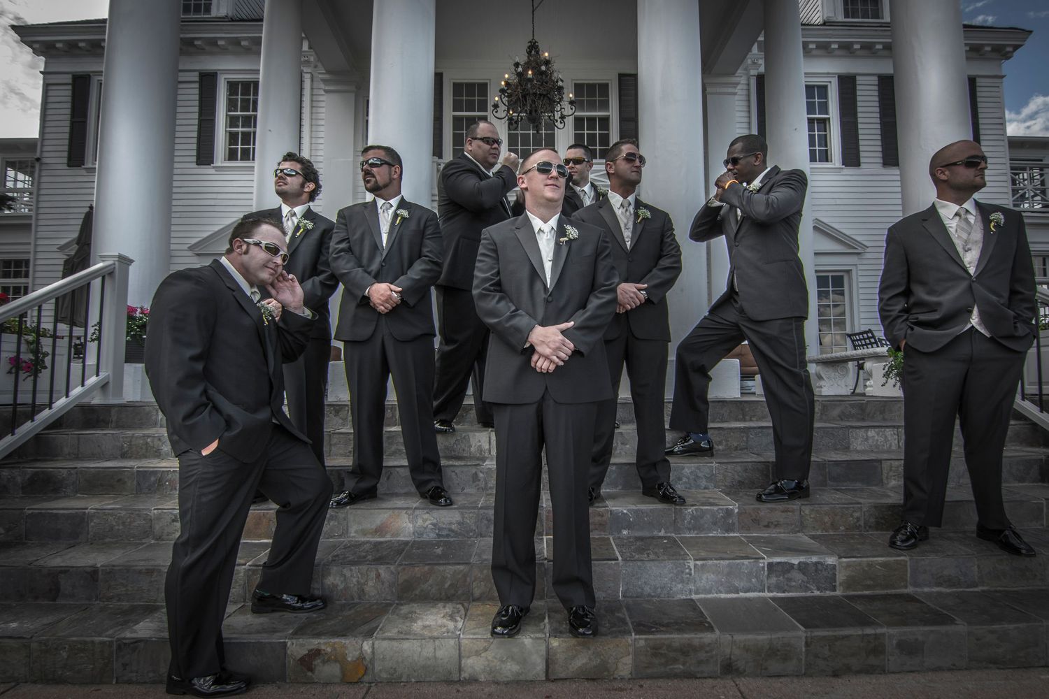 Dramatic black and white photo of groomsmen in suits striking poses on grand building steps.