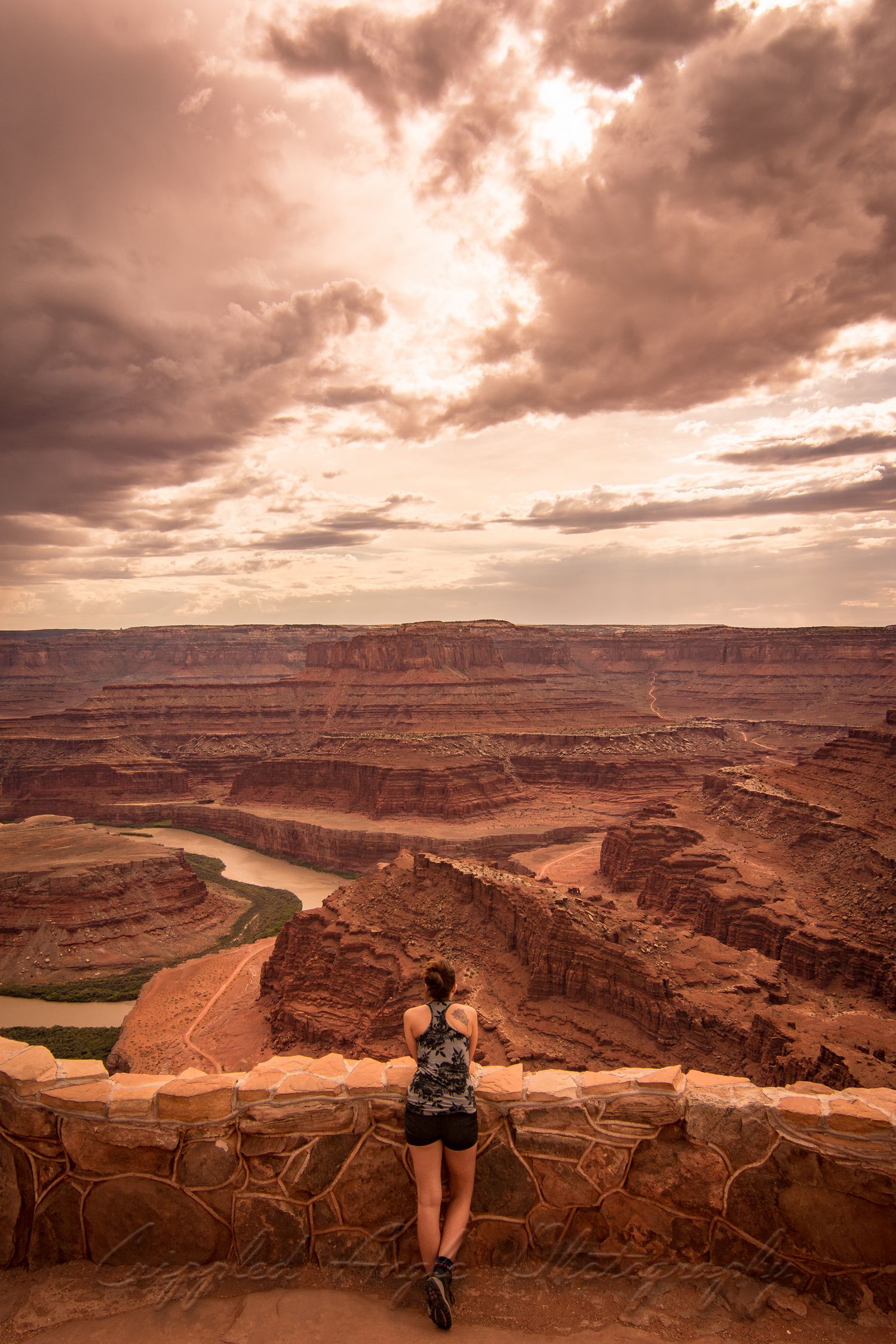 Scenic overlook of a winding river canyon with red rock formations under dramatic stormy skies.