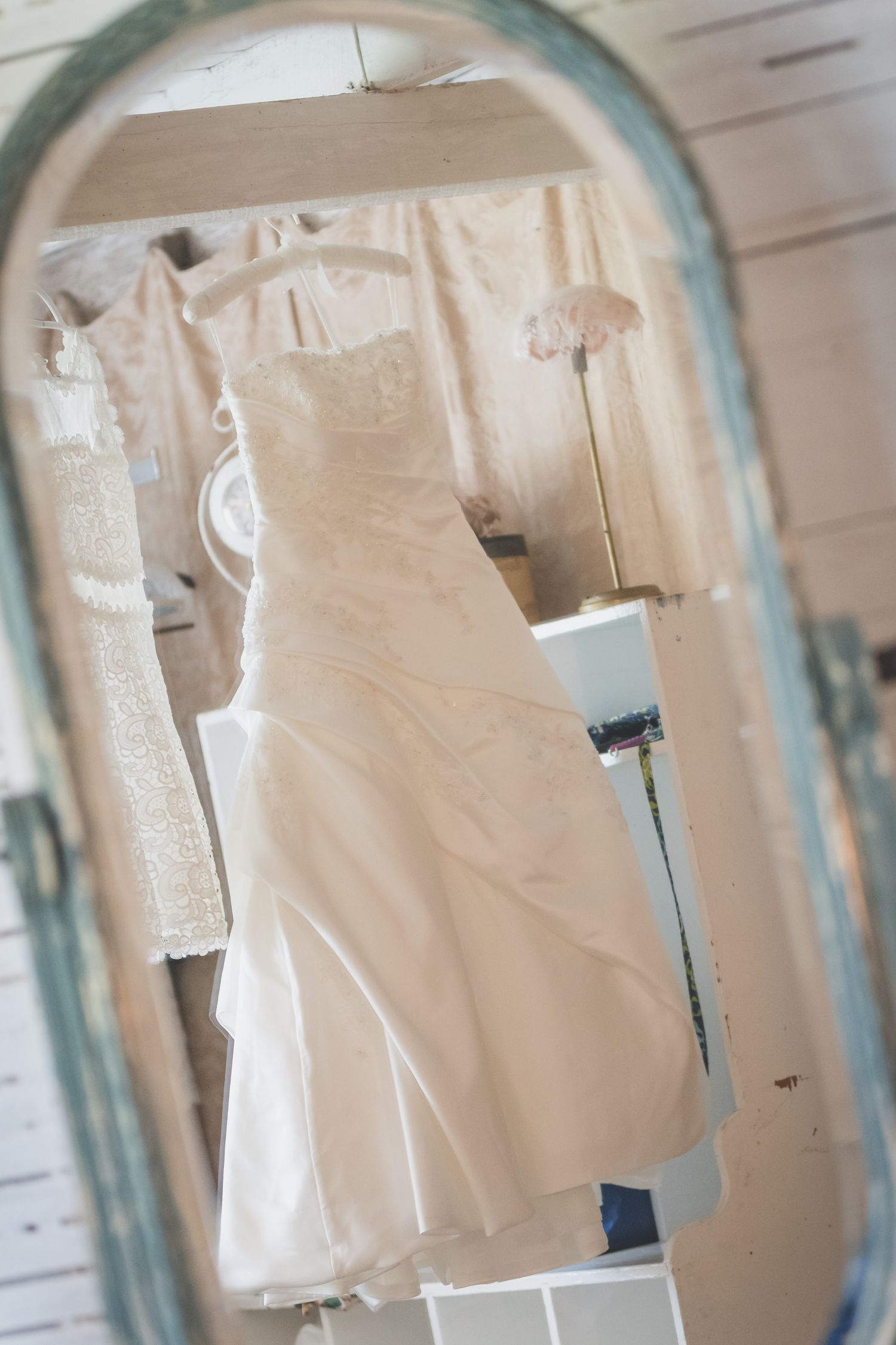 White wedding dress displayed in vintage mirror frame against rustic background.
