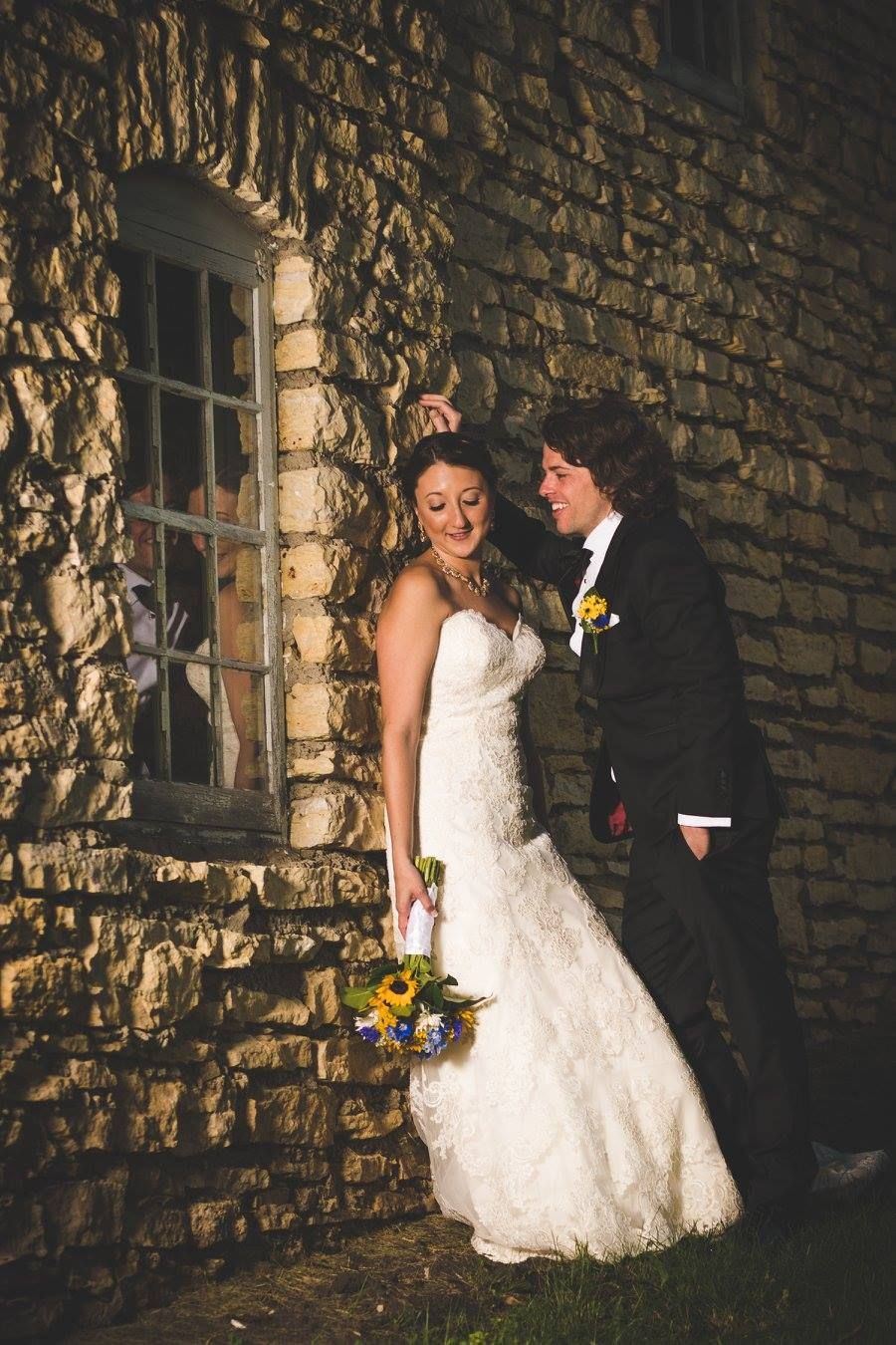 A couple shares an intimate moment against a rustic stone wall with vintage window.