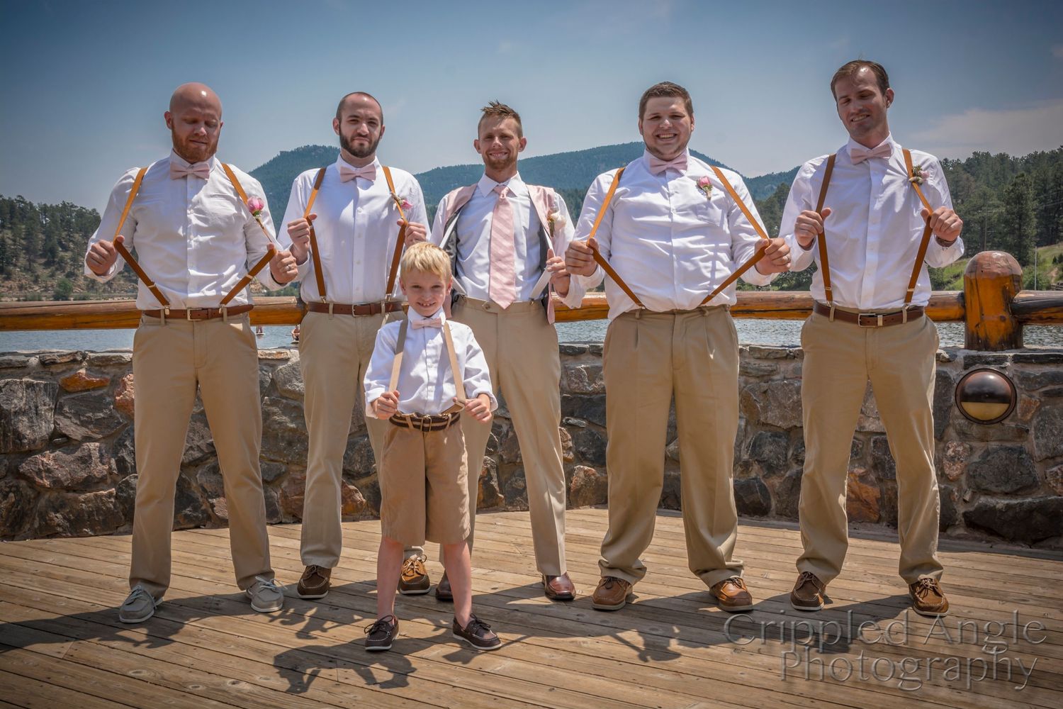 Groomsmen in white shirts and khakis pose with young ring bearer on outdoor deck.