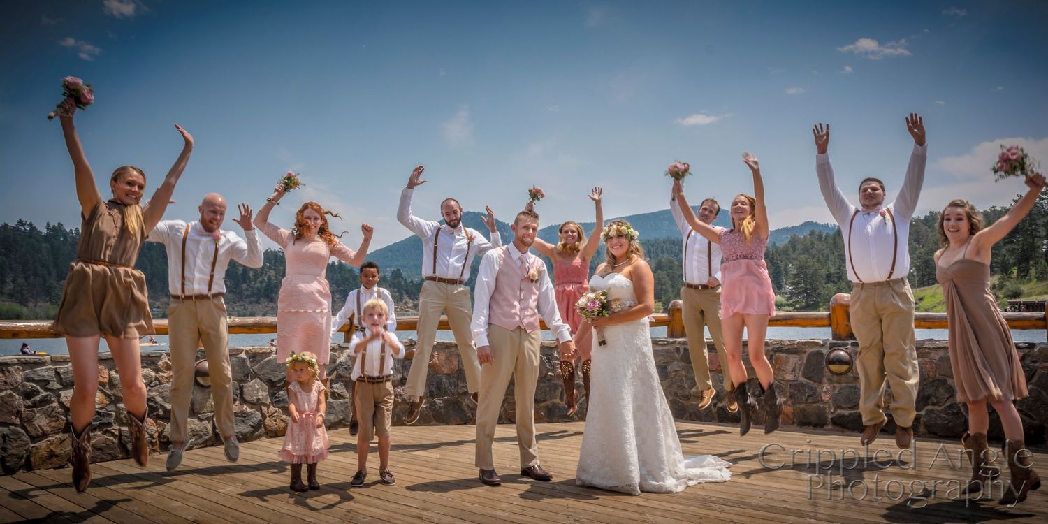 Wedding party celebrates with arms raised against scenic mountain landscape.