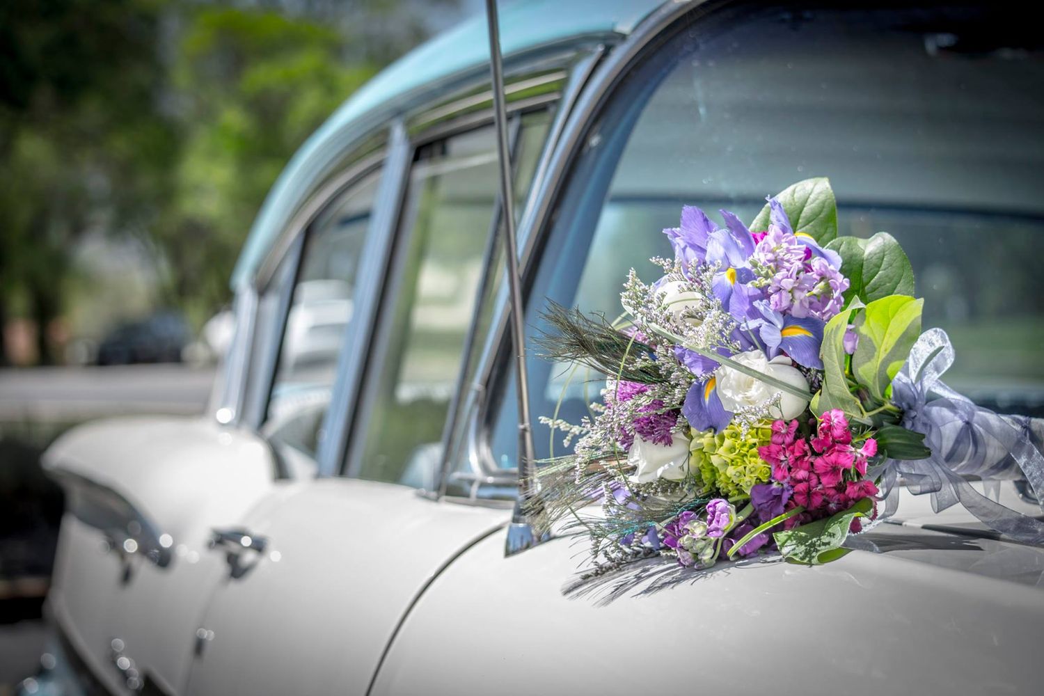 A colorful purple and pink wedding bouquet rests on a classic vintage car.