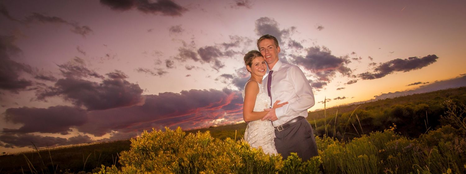 A romantic sunset wedding photo on a hilltop with dramatic pink and orange clouds in the background.