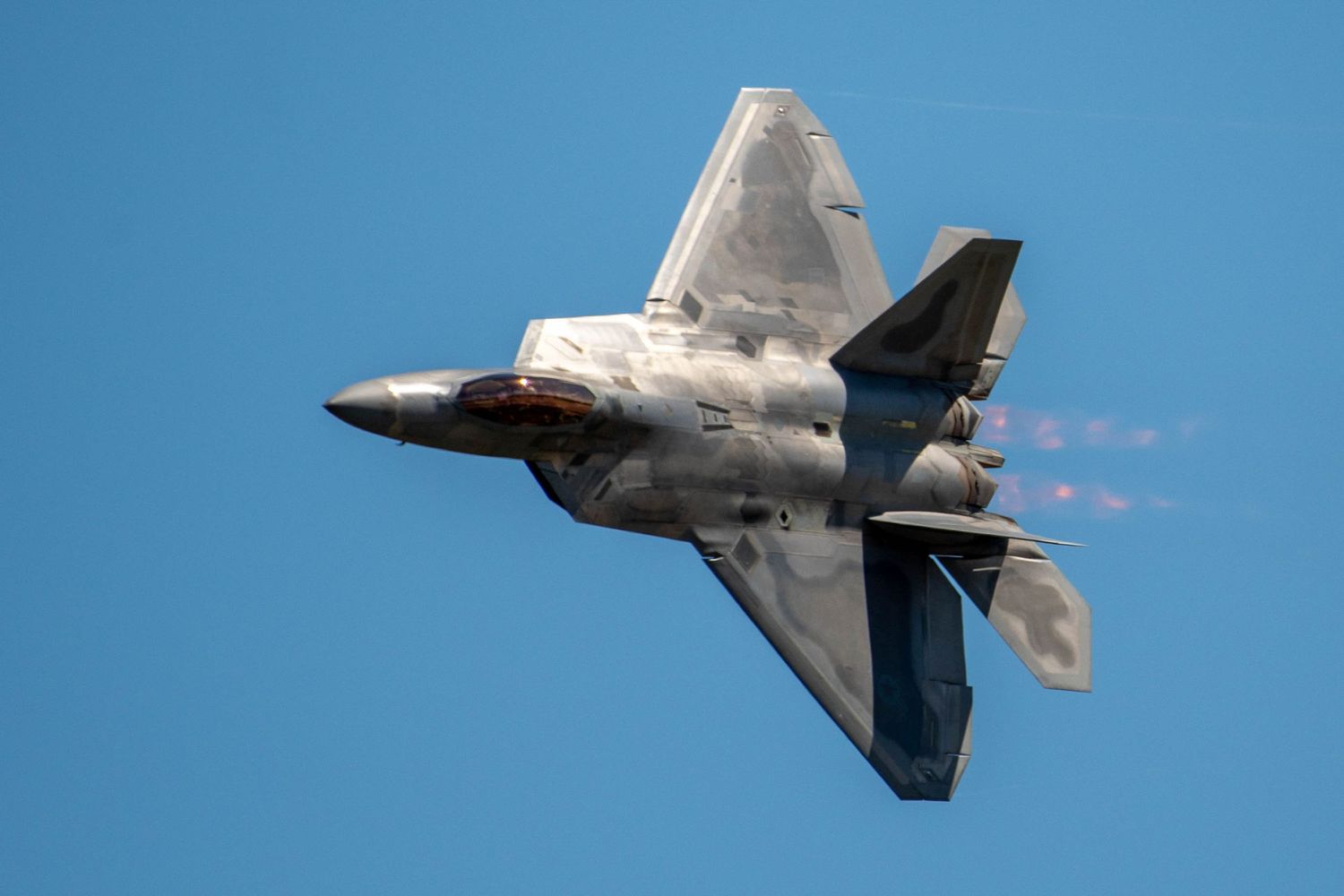 F-22 Raptor stealth fighter jet performing high-speed maneuver with vapor trails in blue sky.