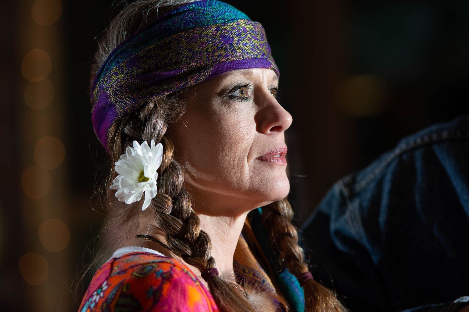 Profile view of someone wearing a colorful bandana and white flower in braided hair at dusk.