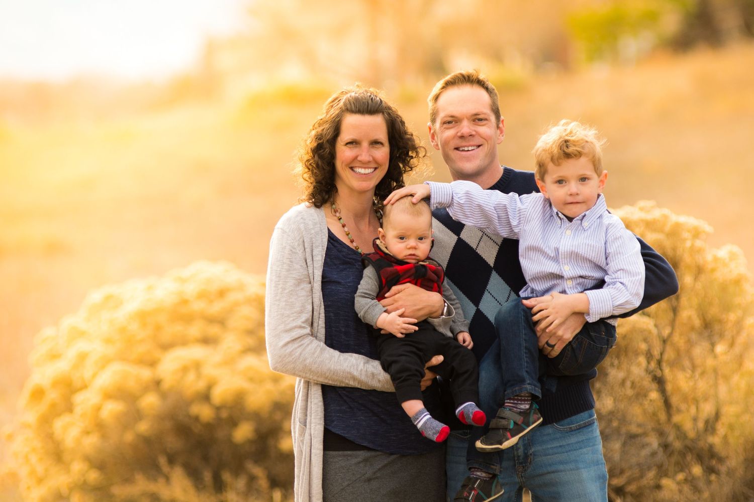 A family poses together outdoors in golden sunlight against a natural backdrop.