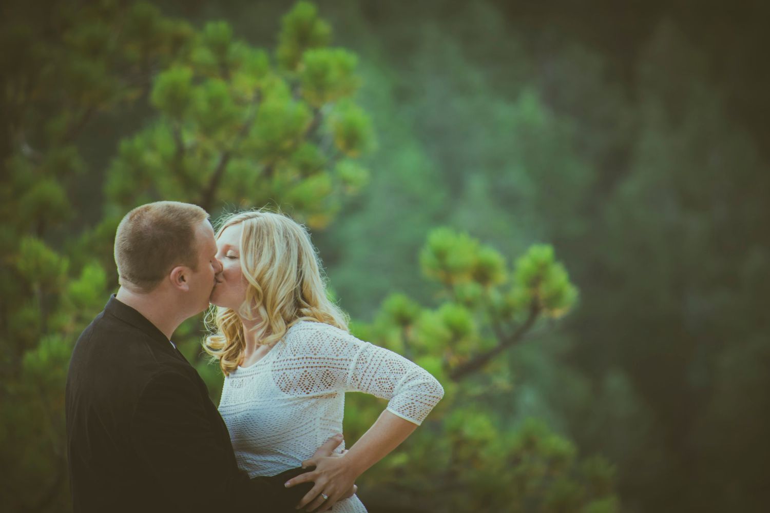 Intimate outdoor portrait of a couple embracing against a blurred green forest backdrop.
