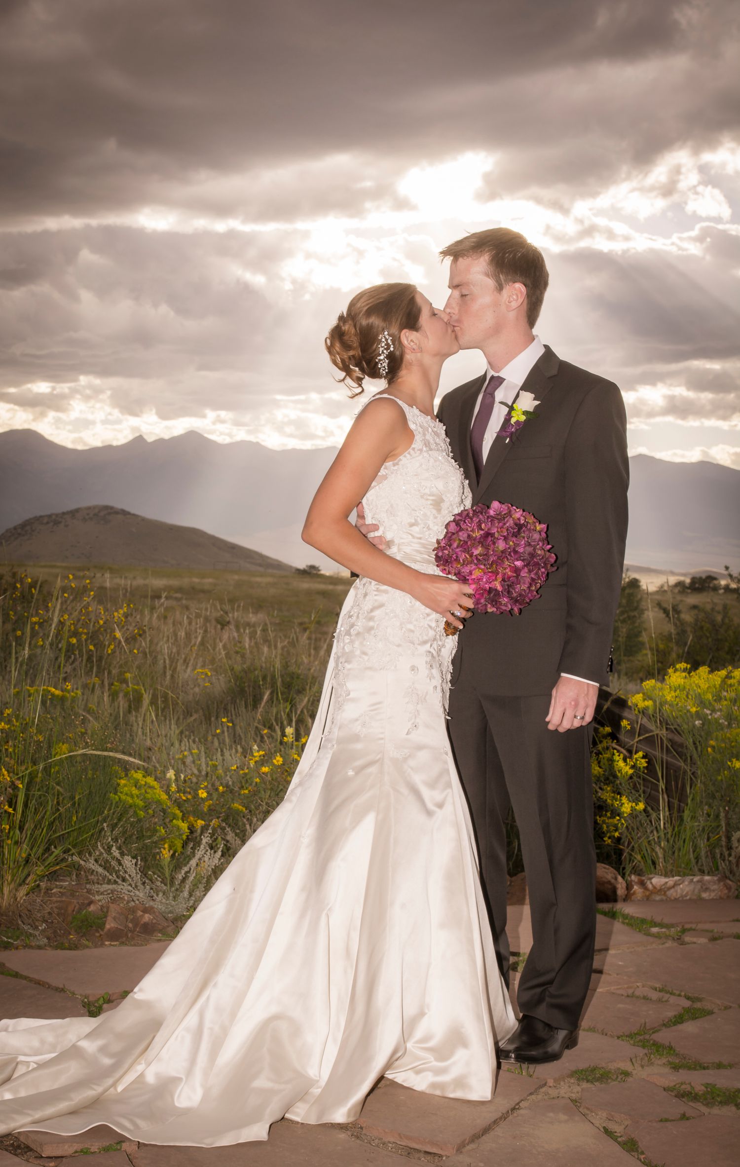 Romantic wedding couple embracing with mountains and dramatic sky in background.