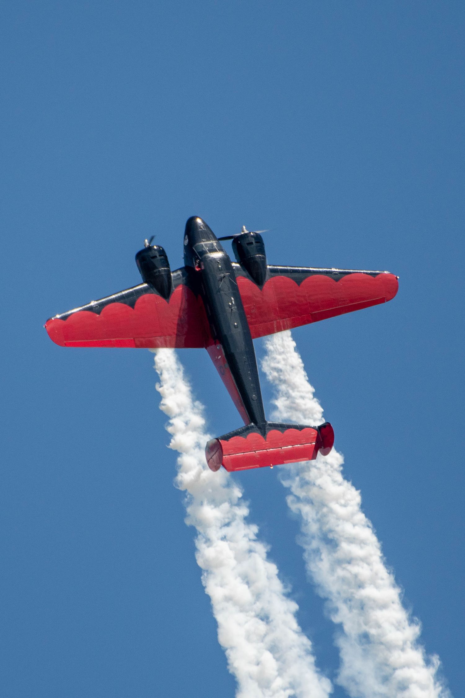 Red vintage aircraft performing aerobatic maneuver with white smoke trails against blue sky.