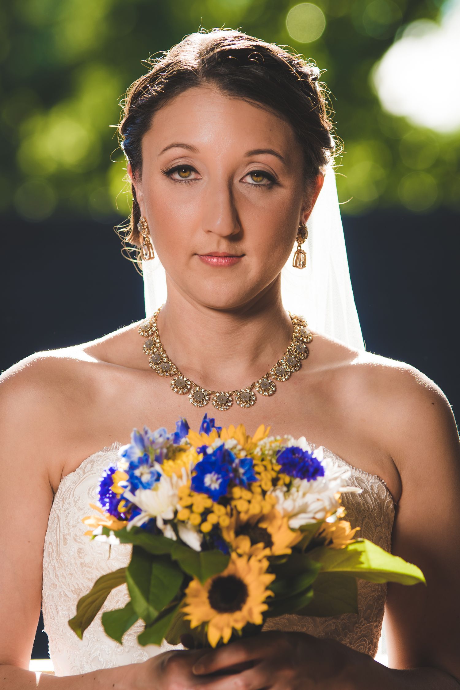 Elegant bride wearing a white strapless gown with sunflower bouquet and ornate gold necklace.