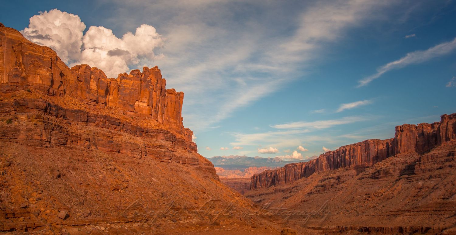 Dramatic red rock cliffs and canyons under fluffy white clouds and blue skies in the American Southwest.