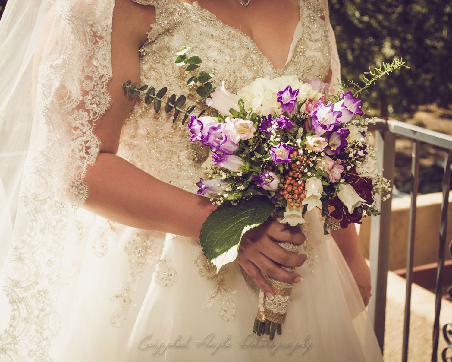 A close-up of a bride holding a purple and white wildflower wedding bouquet.