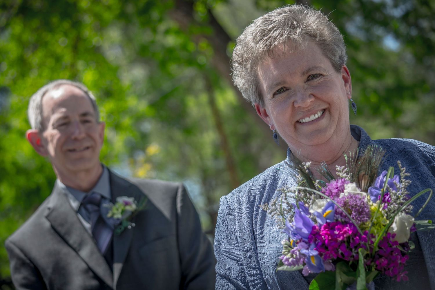 Outdoor wedding portrait with bright purple floral bouquet in foreground.