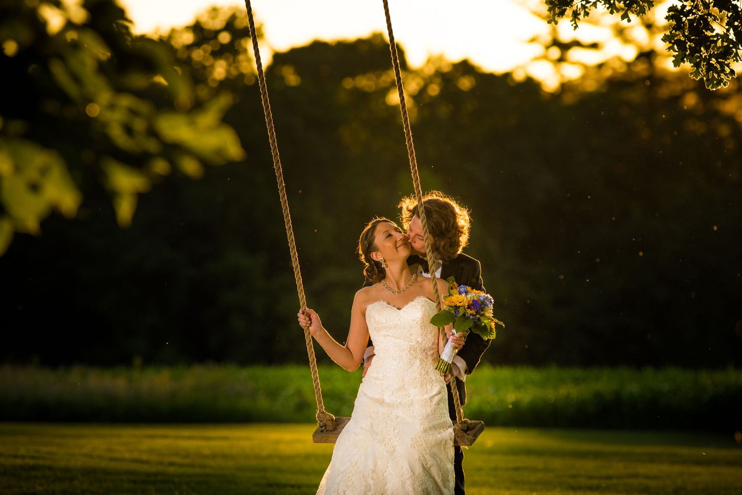 Romantic couple on swing at sunset in wedding attire.