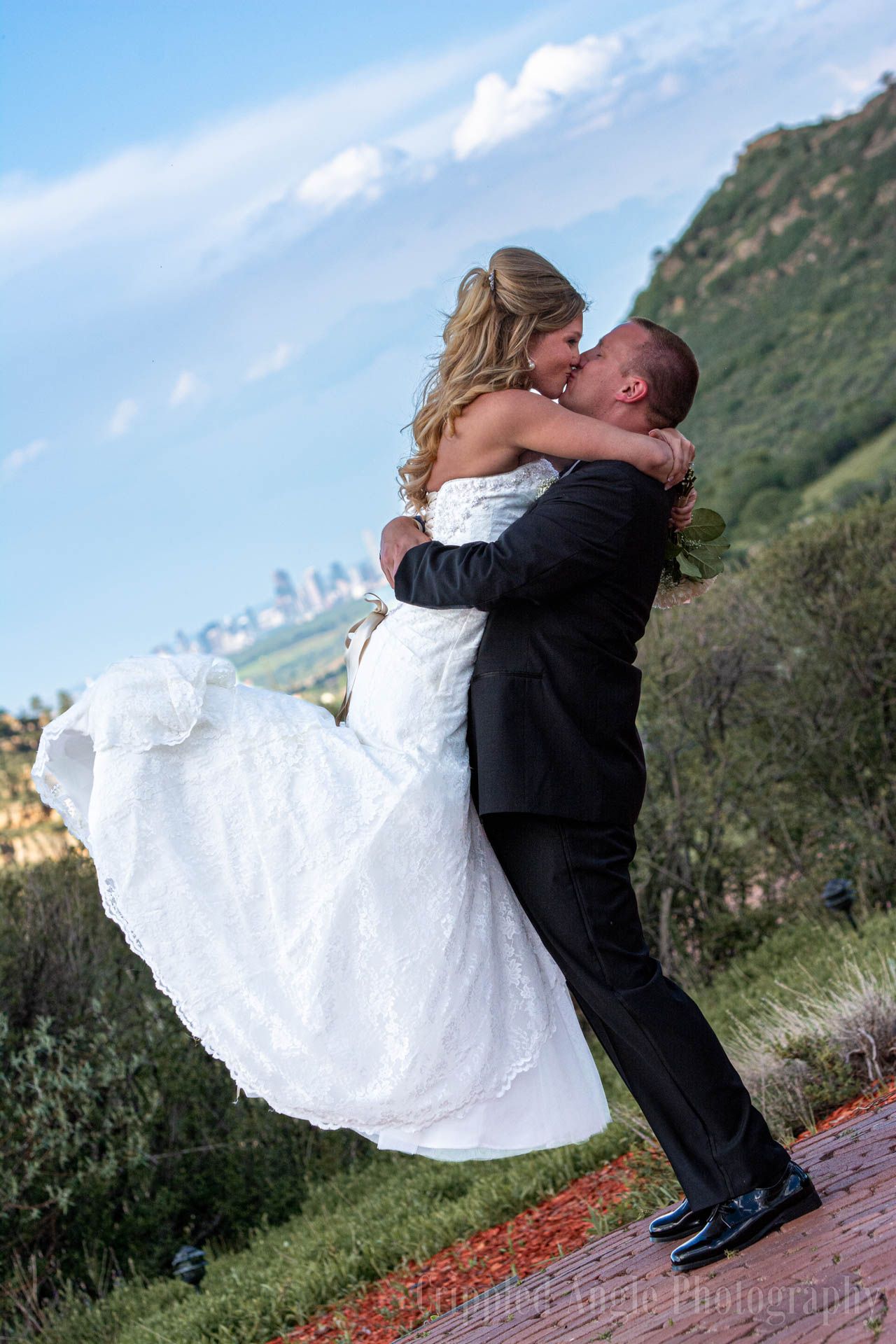 Romantic wedding photo of couple embracing on mountainside with dramatic landscape.
