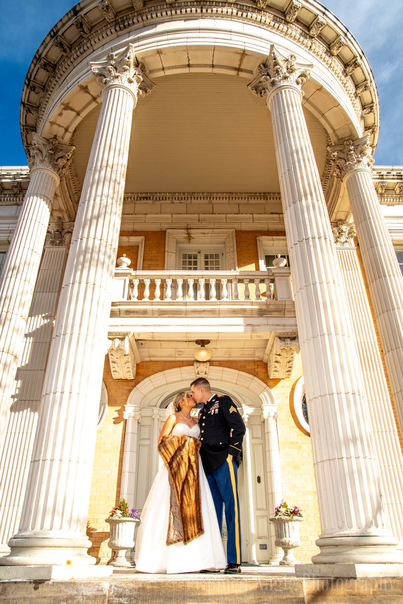 A wedding couple poses under grand classical columns at an elegant building entrance.