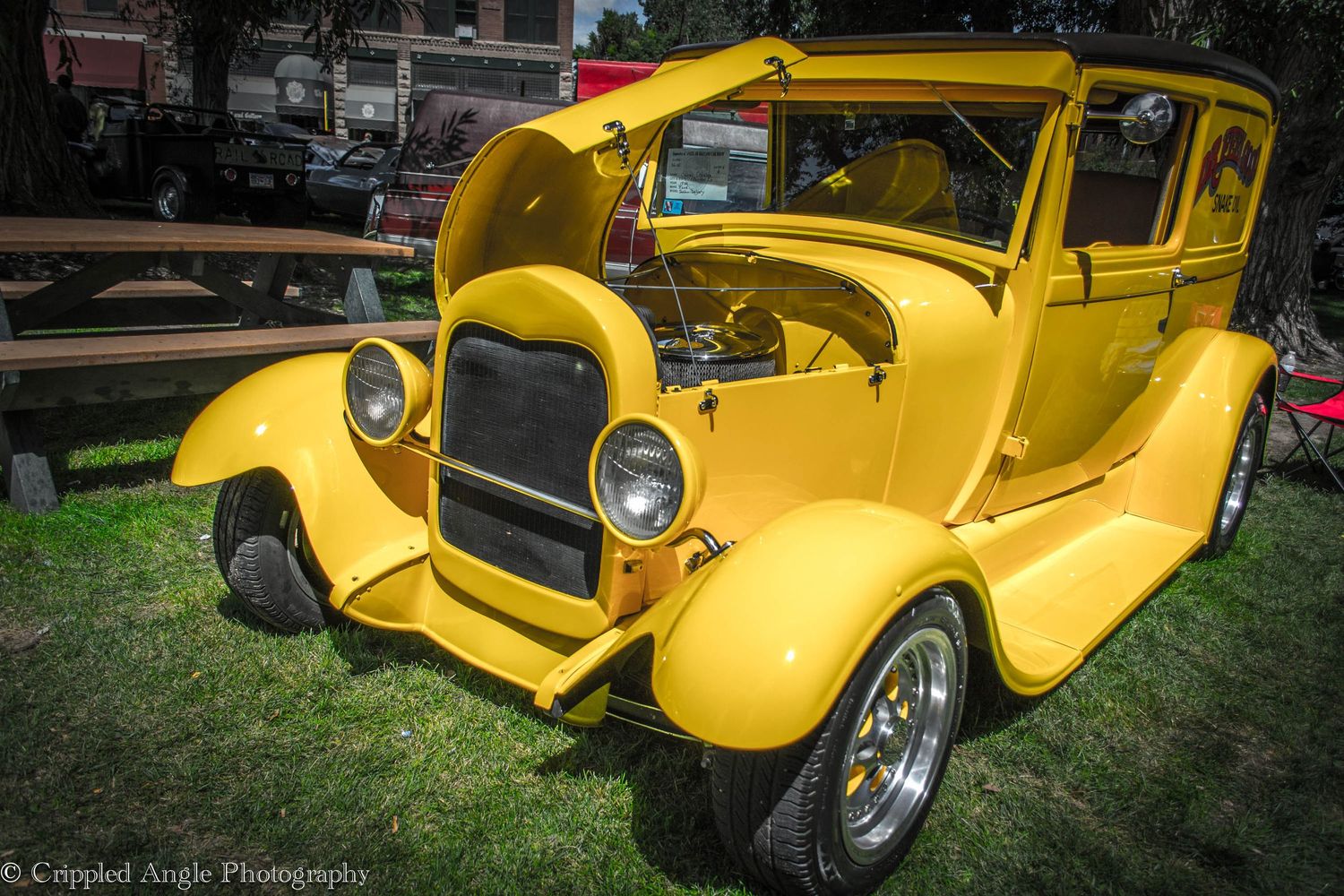 Bright yellow vintage hot rod with open hood on display at car show.