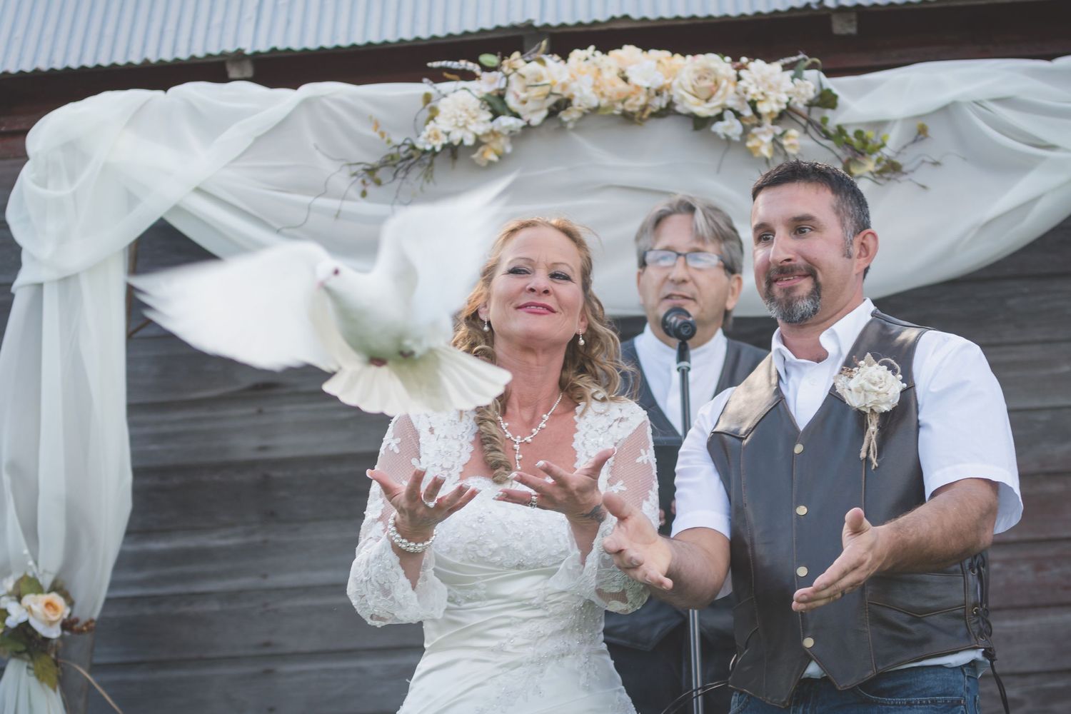 A couple releasing white doves during their outdoor wedding ceremony under a floral arch.