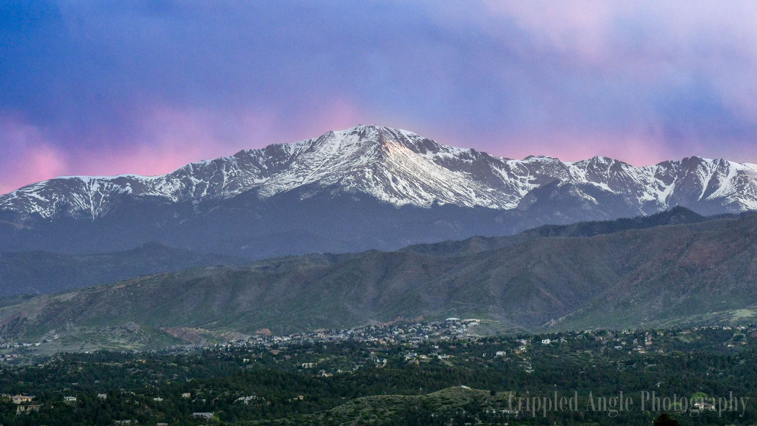 Snow-capped Pikes Peak mountain range under a dramatic purple sunset sky in Colorado.