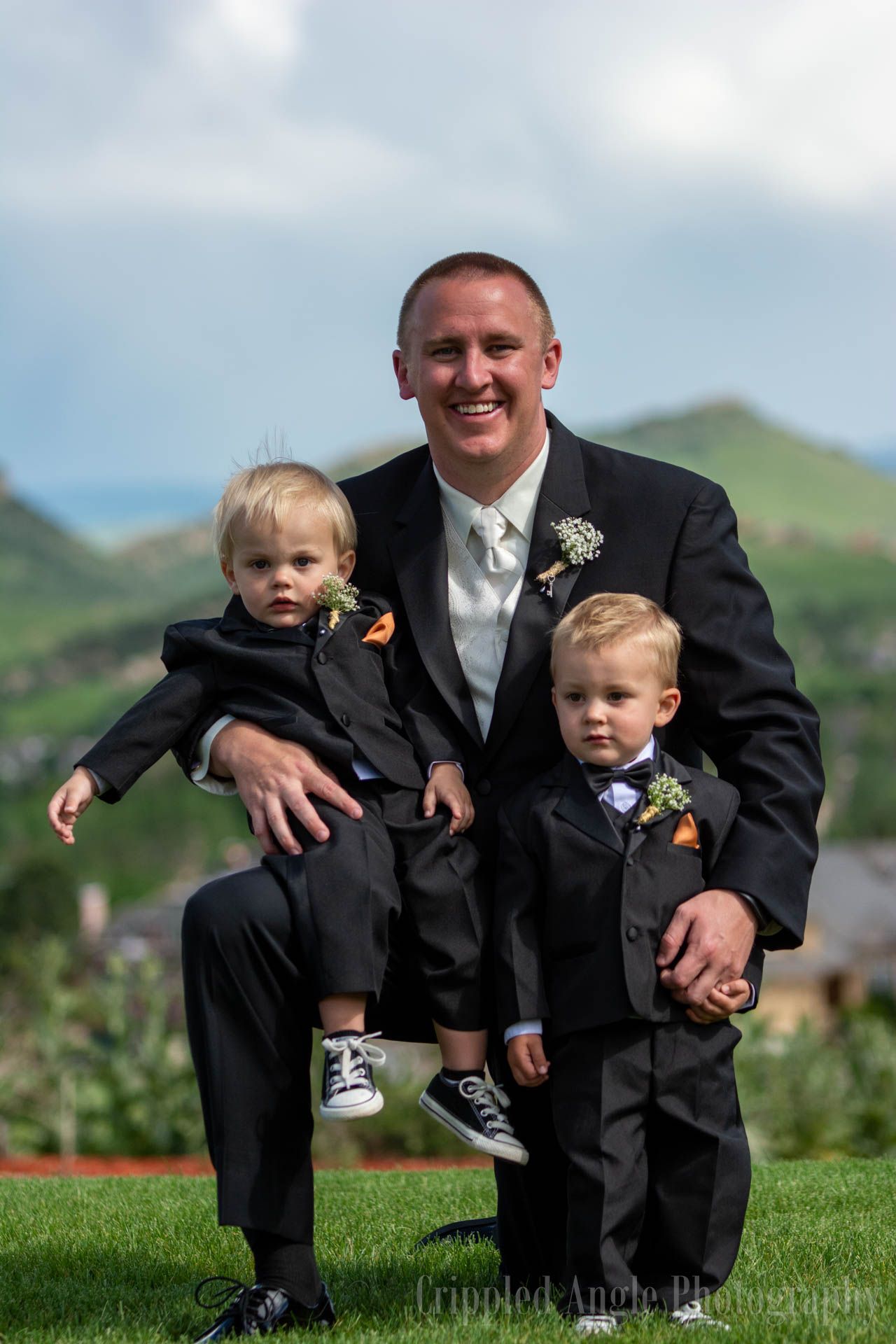 A formal outdoor family portrait taken on a grassy hillside with mountains in the background.