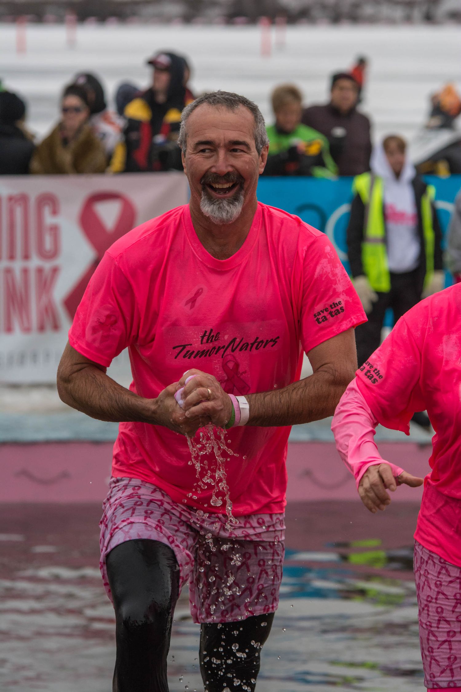 Participant in pink shirt splashing through water during cold plunge event.