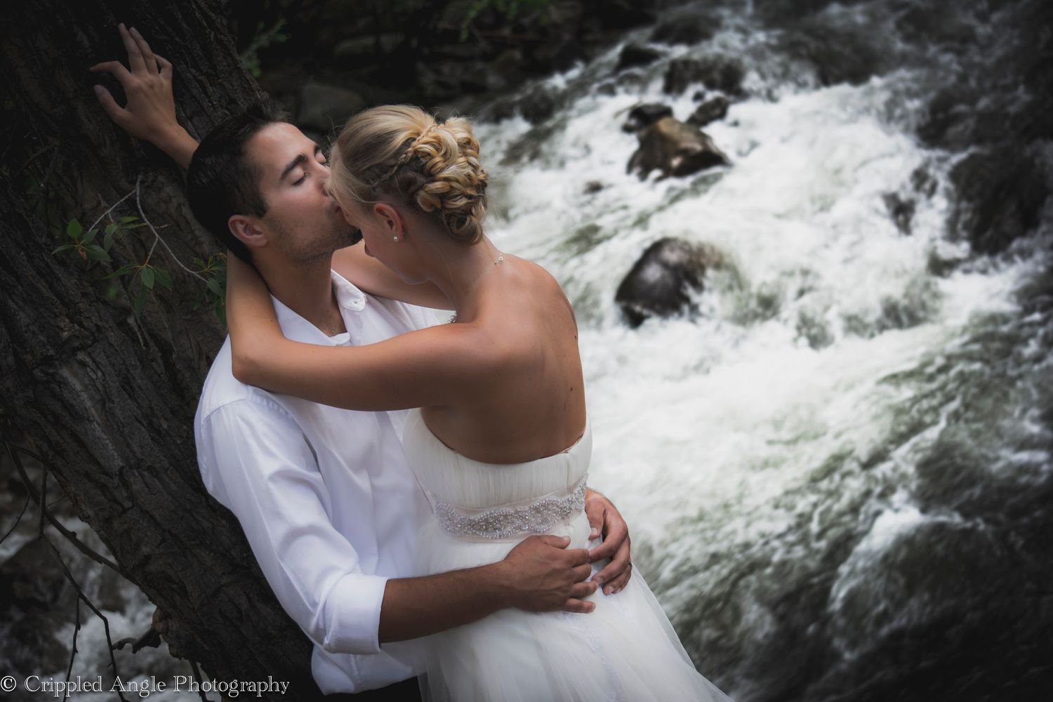 Couple sharing romantic moment by rushing waterfall in wedding attire.
