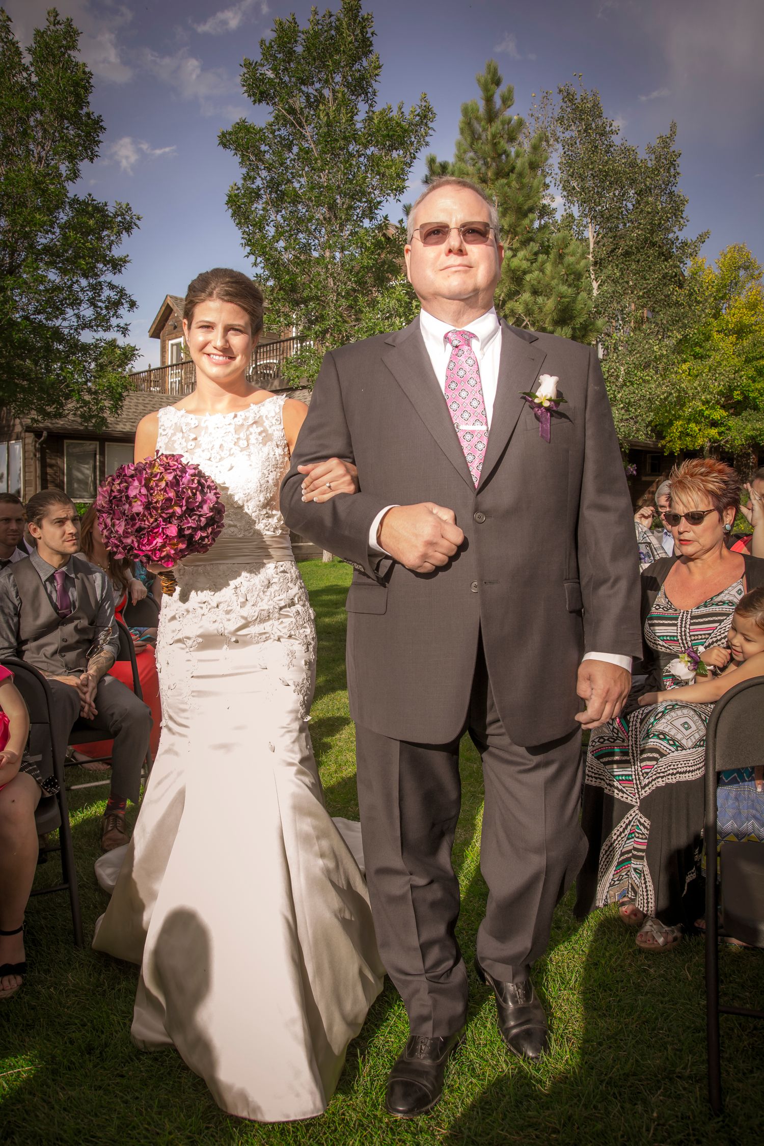 Wedding ceremony on a sunny lawn with attendees watching from their seats.