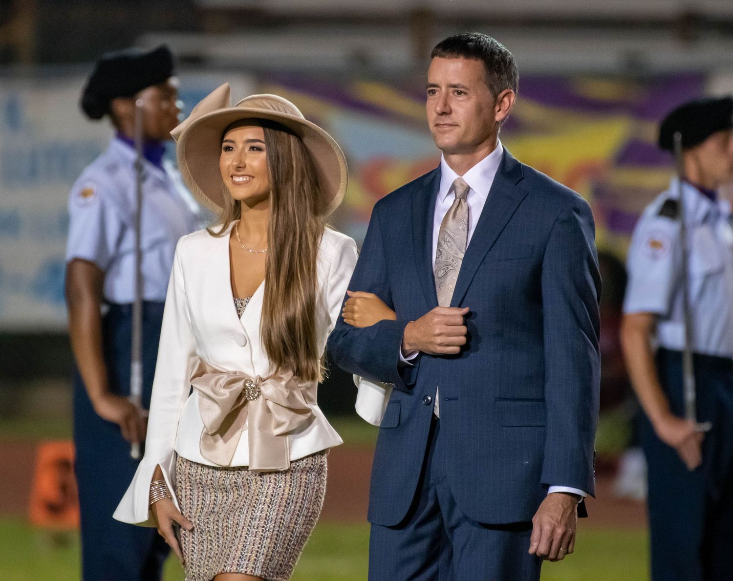 Formal couple stands during ceremonial event at sports venue.