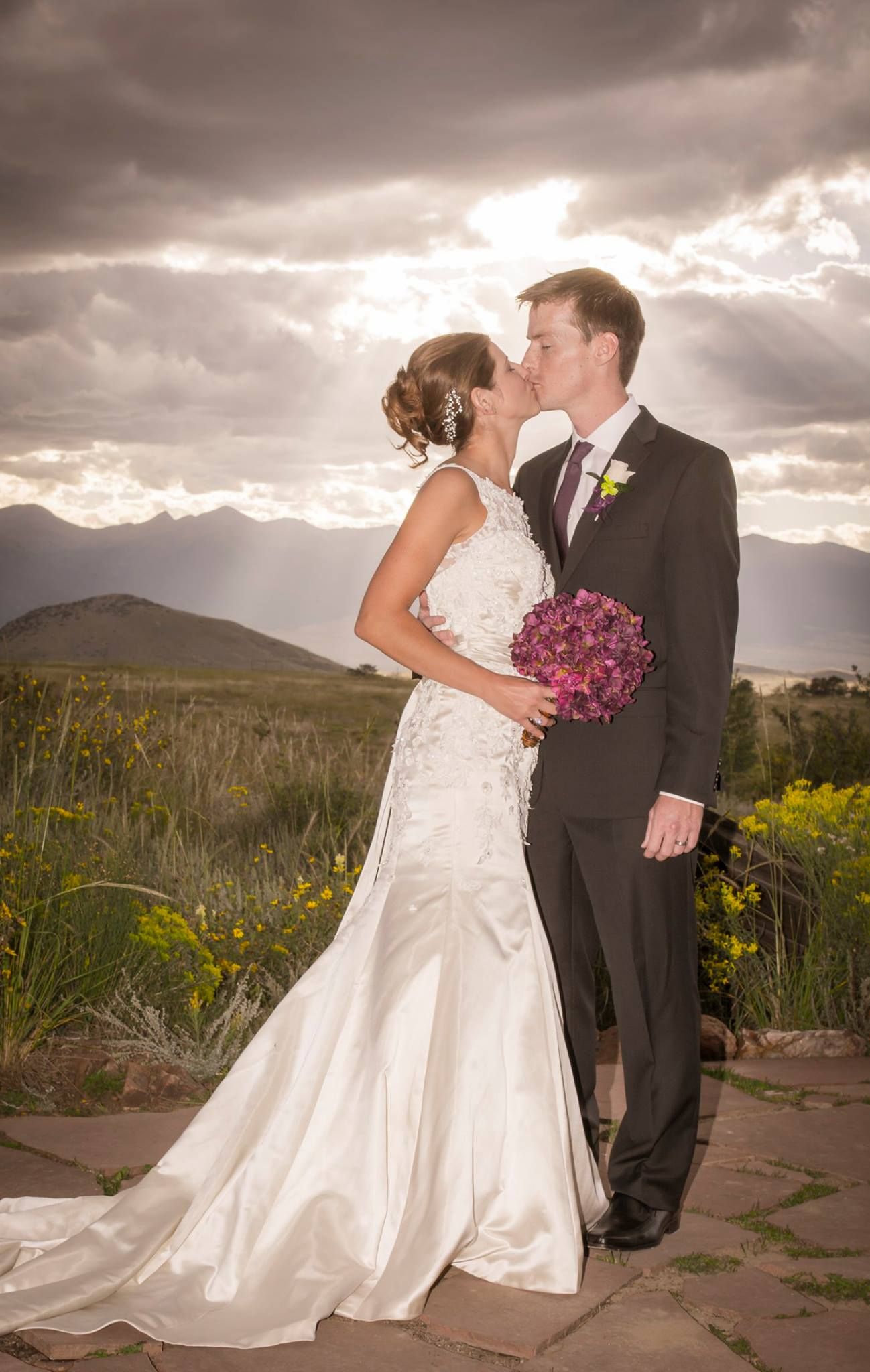 A wedding moment captured against mountain peaks with dramatic sunbeams breaking through clouds.