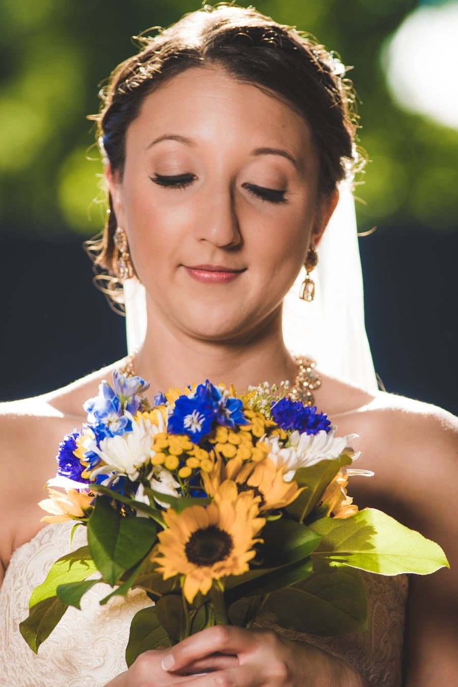 A bride holding a bouquet of sunflowers and blue flowers with eyes closed.