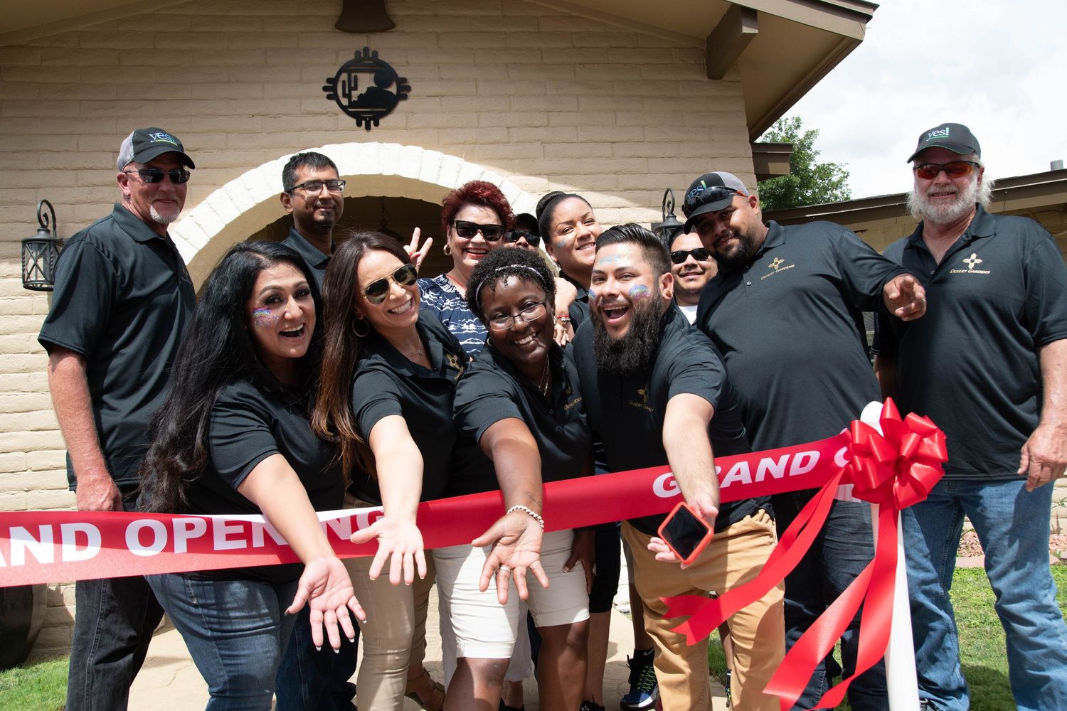 Team gathered around red grand opening ribbon for celebration photo.