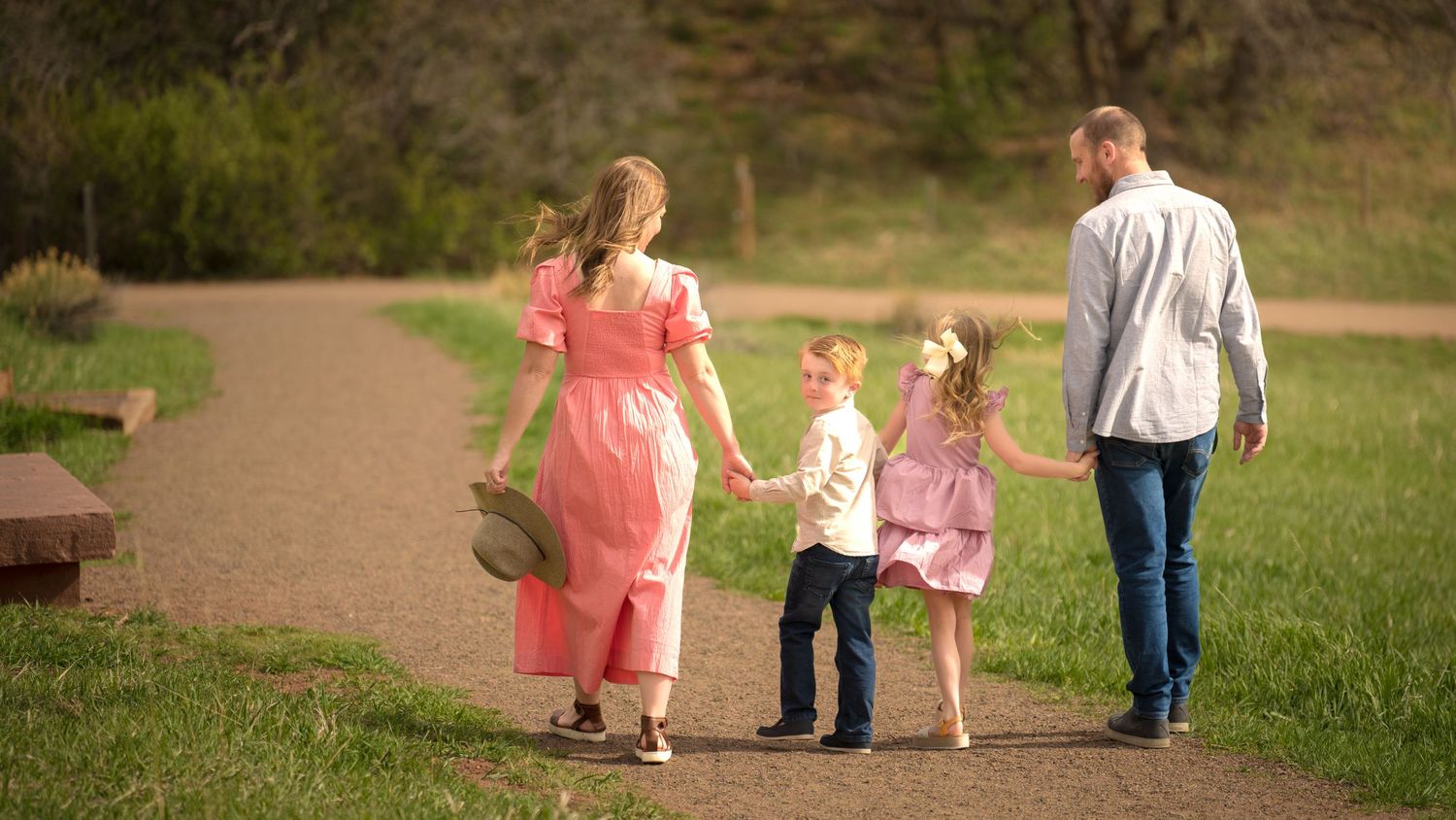 A family walks together on a winding path through a park on a sunny afternoon.