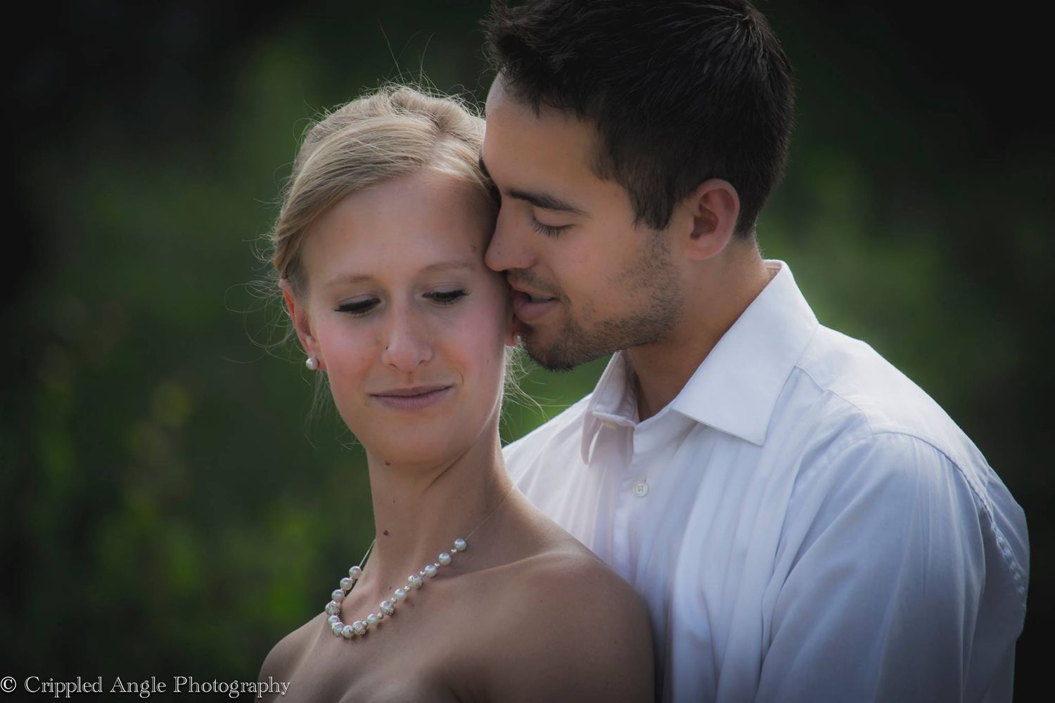 A tender embrace captured in soft lighting with elegant wedding attire and natural background.