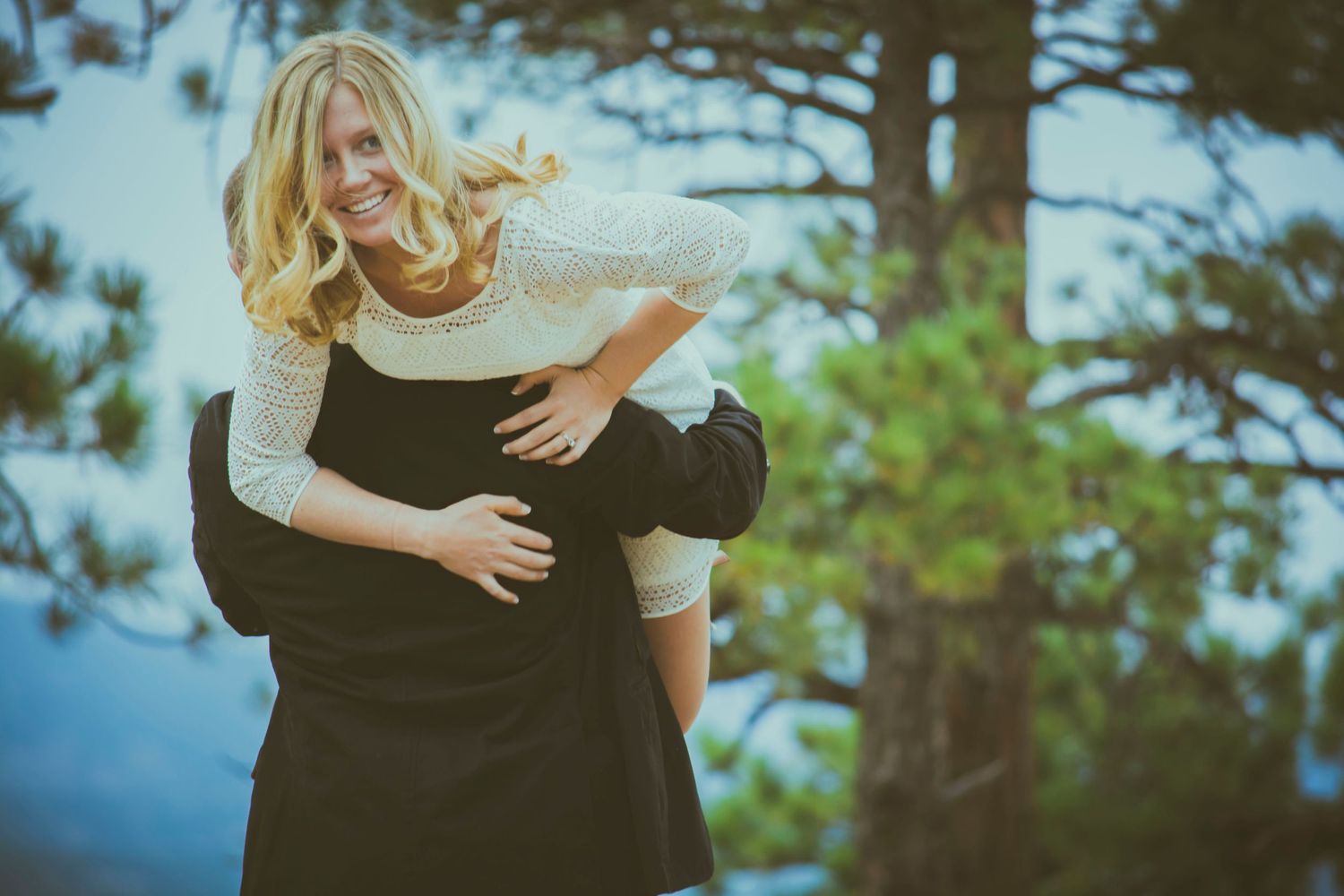Romantic engagement photo of couple embracing against blurred nature background.