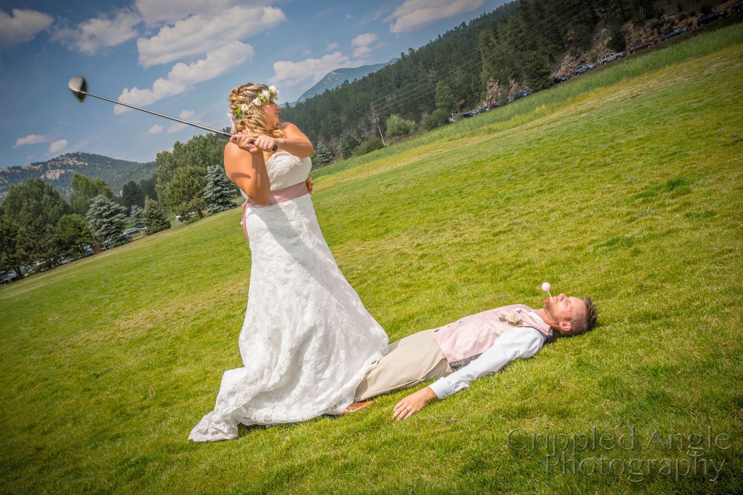 Playful wedding photo of bride taking celebratory drink while groom lies on grass.