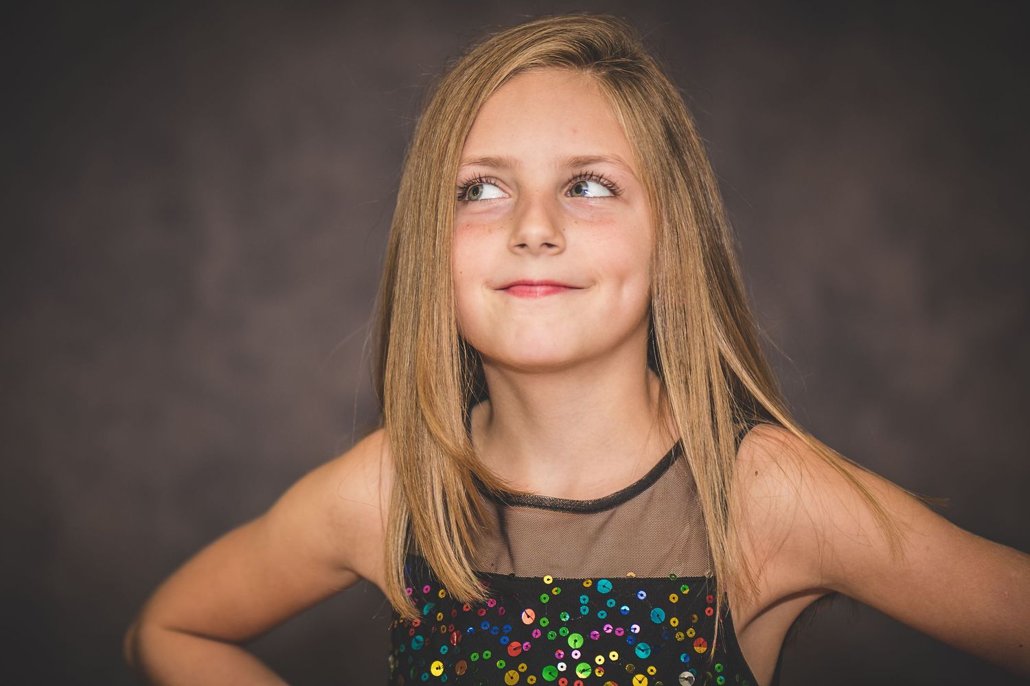 Studio portrait with sparkly dress against dark background showing upward glancing pose.