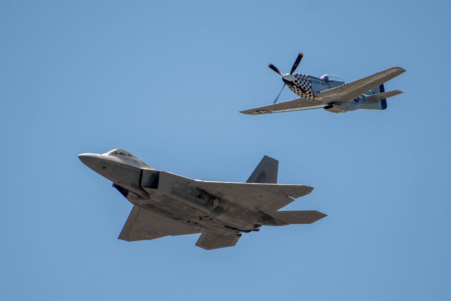 F-35 fighter jet flying alongside vintage P-51 Mustang warbird in clear blue sky.