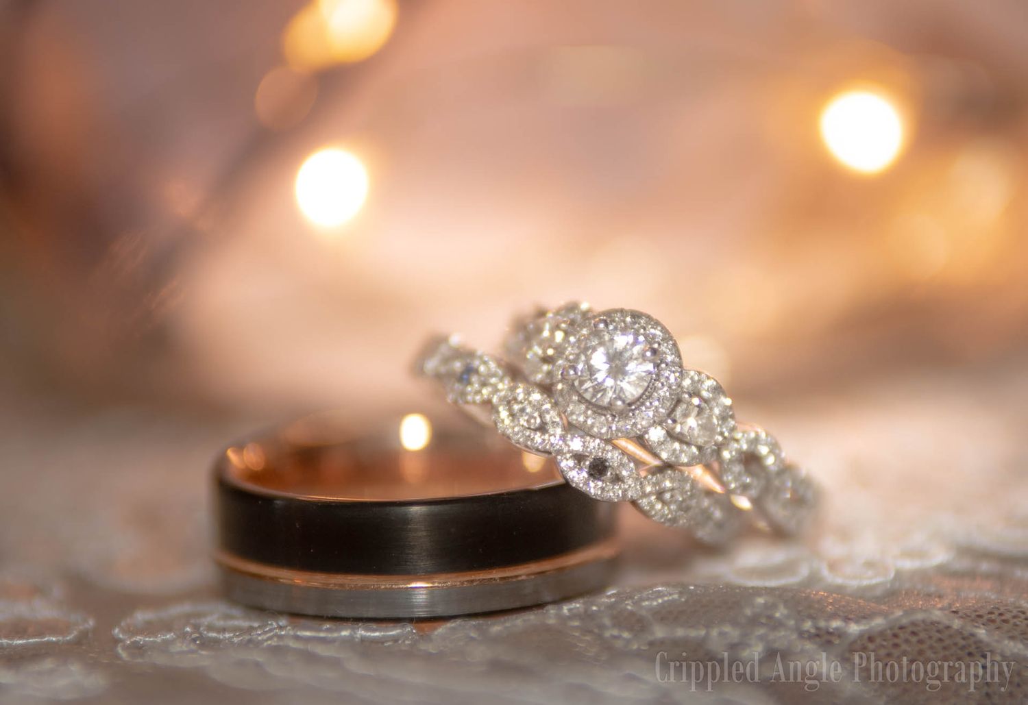 Close-up of diamond engagement ring and wedding band on textured fabric with bokeh lighting.