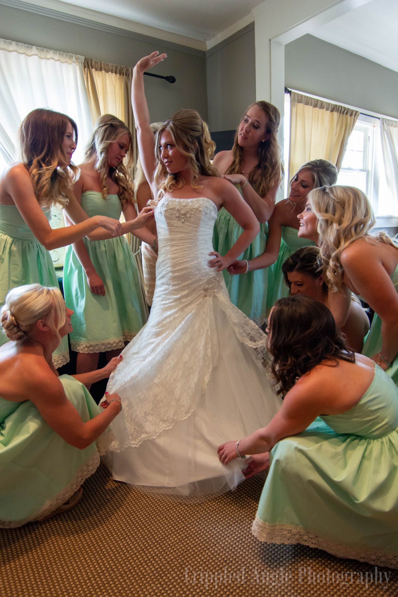 Bridesmaids in mint green dresses help adjust bride's wedding gown.
