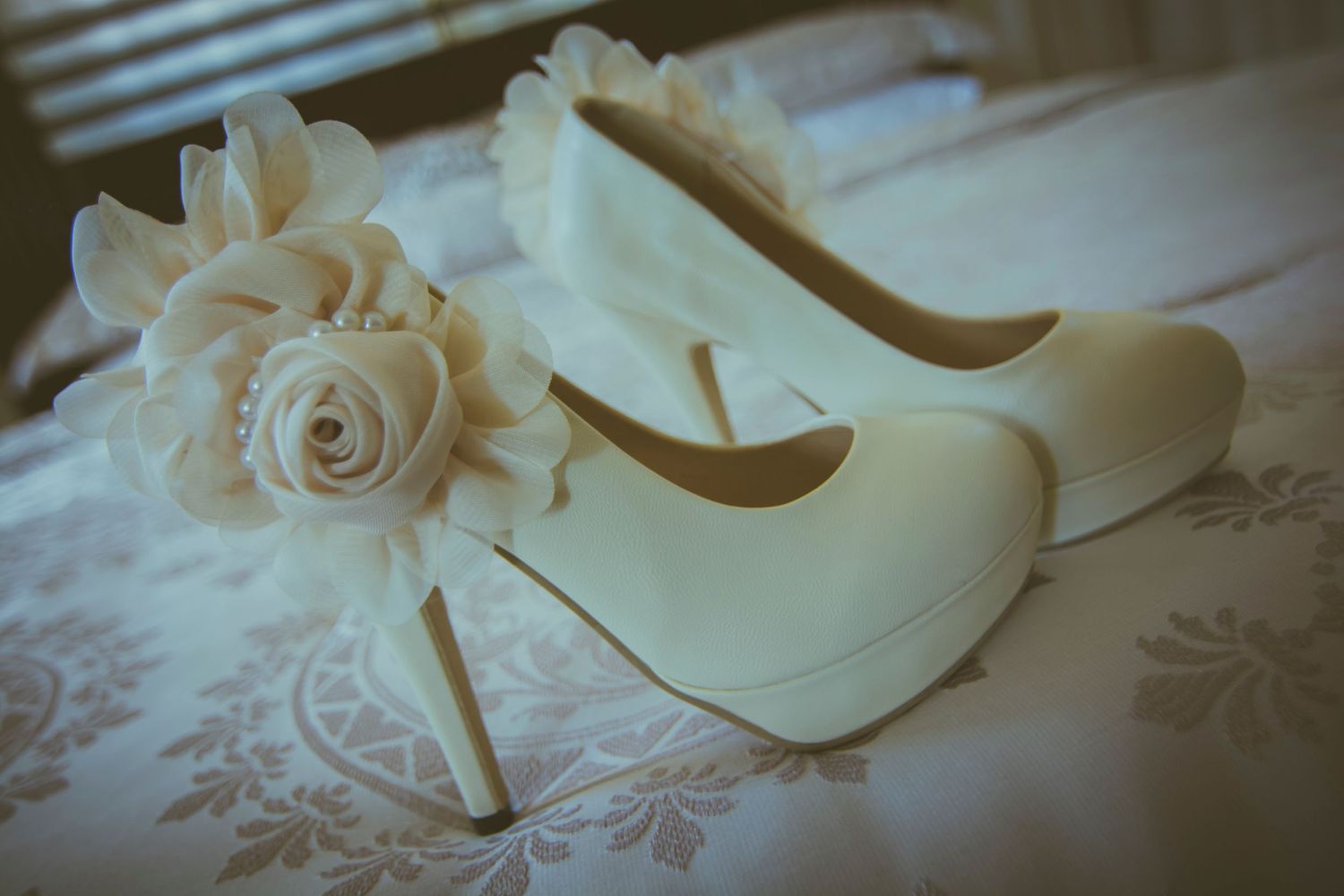 Elegant white bridal heels with floral detail on lace tablecloth.
