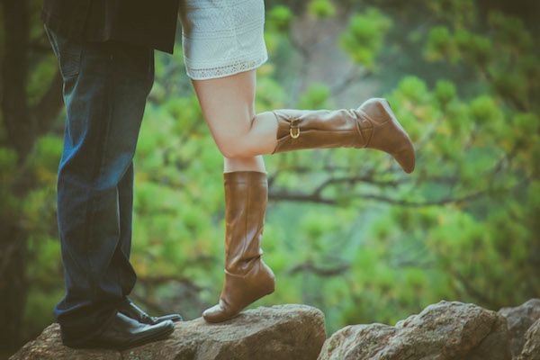 Romantic couple's feet standing on rocks with brown boots against green natural background.