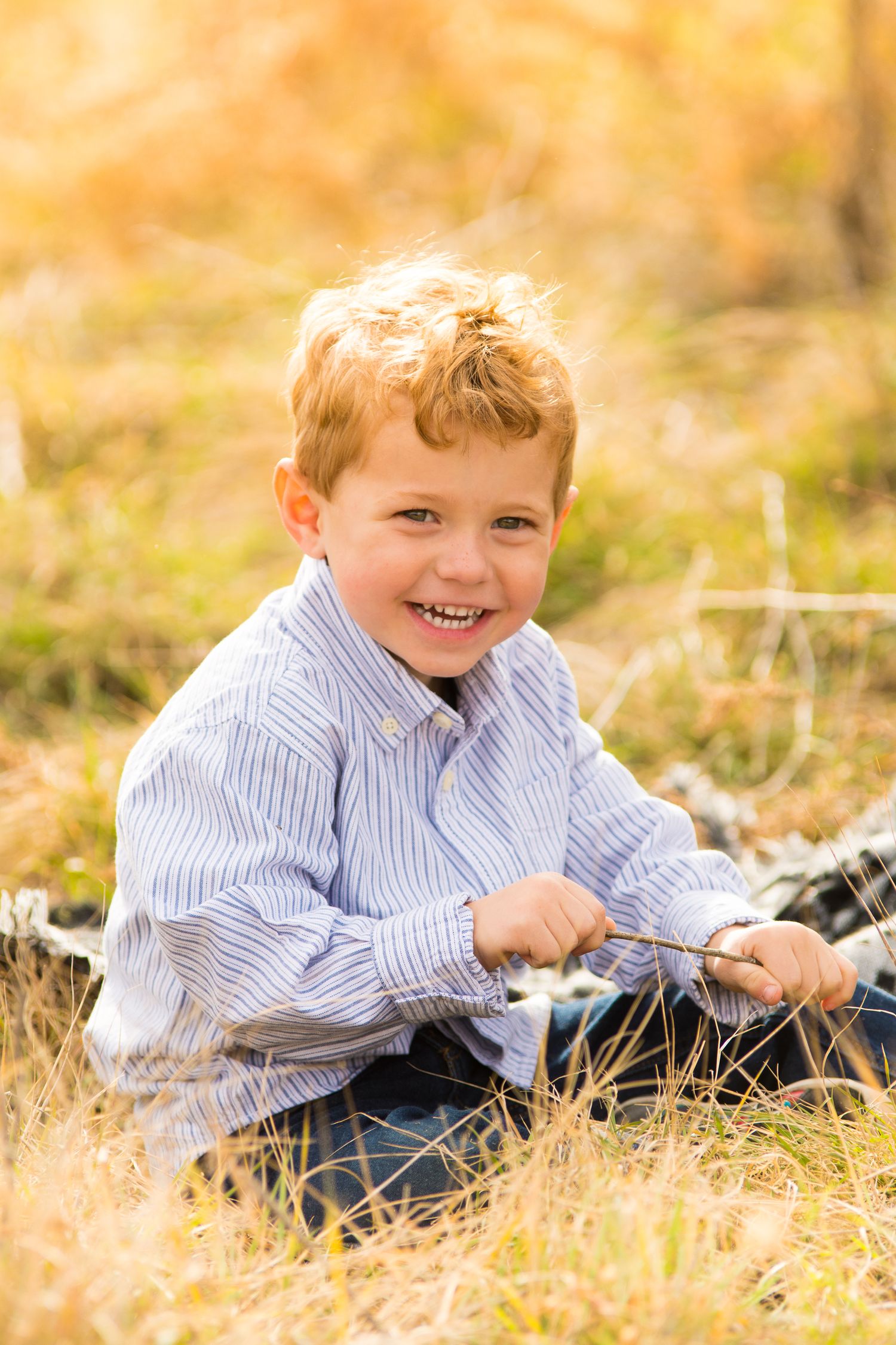 Young child sits in tall grass during golden hour photo session.