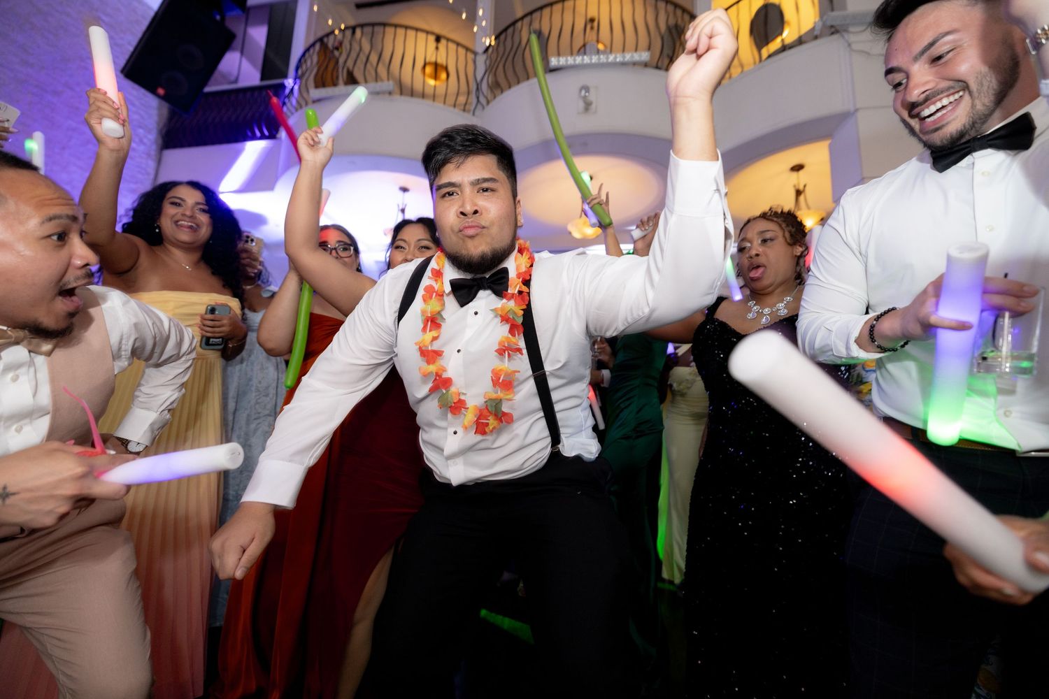 A lively wedding reception dance party with people dancing and celebrating under decorative lighting.